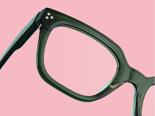 Gros plan sur des lunettes carrées en vert olive translucide inclinées sur fond rose clair.