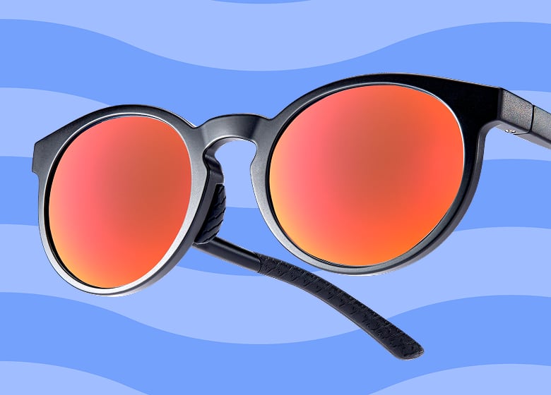 Matte black round sunglasses with vibrant red mirrored lenses floating over a sunny beach and ocean background under a white "Zunscreen" logo.