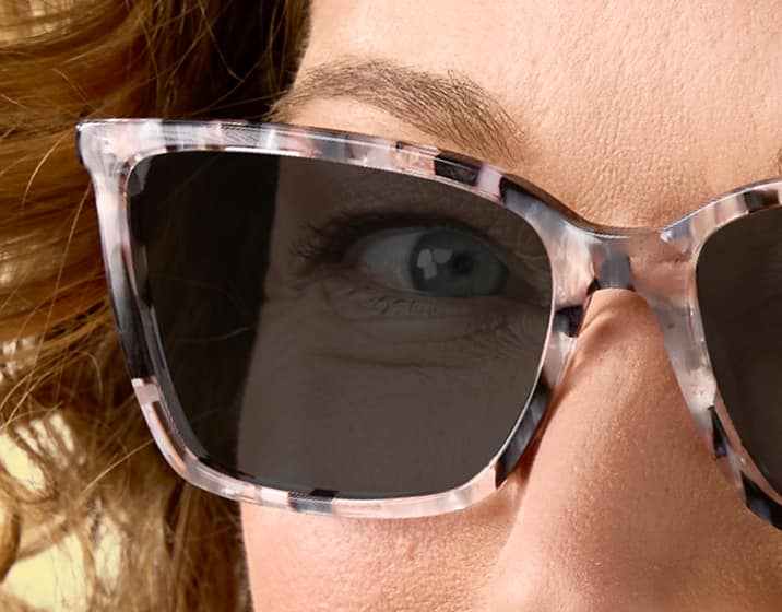 Close up of a woman wearing pink tortoiseshell cat-eye Zenni sunglasses with dark gray lenses.