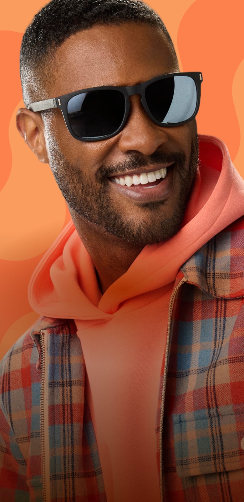 A man with buzzed hair and a beard wearing black square Zenni sunglasses. Wavy orange stripe background.