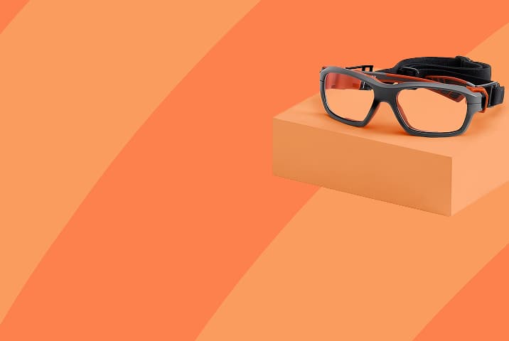 Gray sports goggles with black and red strap on an orange background.