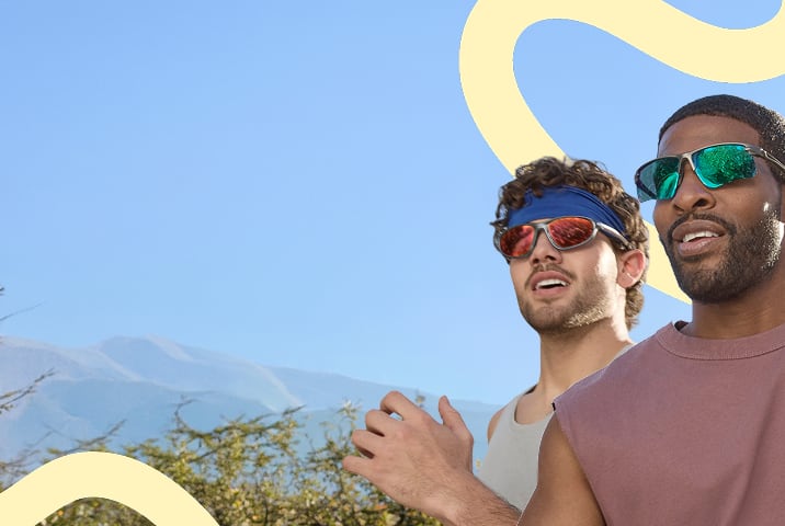 Dos hombres con ropa deportiva y Lentes de Sol deportivos Zenni sobre un fondo de cielo azul con rayas onduladas amarillas.
