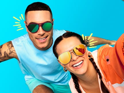 Two people smiling in colorful sunglasses posing against a blue backdrop with playful yellow doodles.