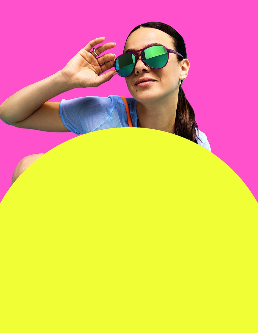 Female model posing in green-mirrored Zunnies Active Style sunglasses against a pink and yellow background.