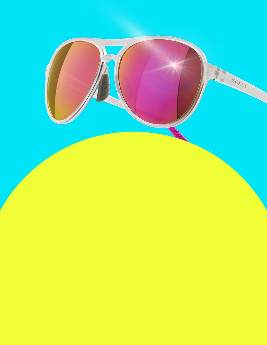 Close-up of white Zunnies Active Style sunglasses with pink polarized lenses on a blue and yellow background.