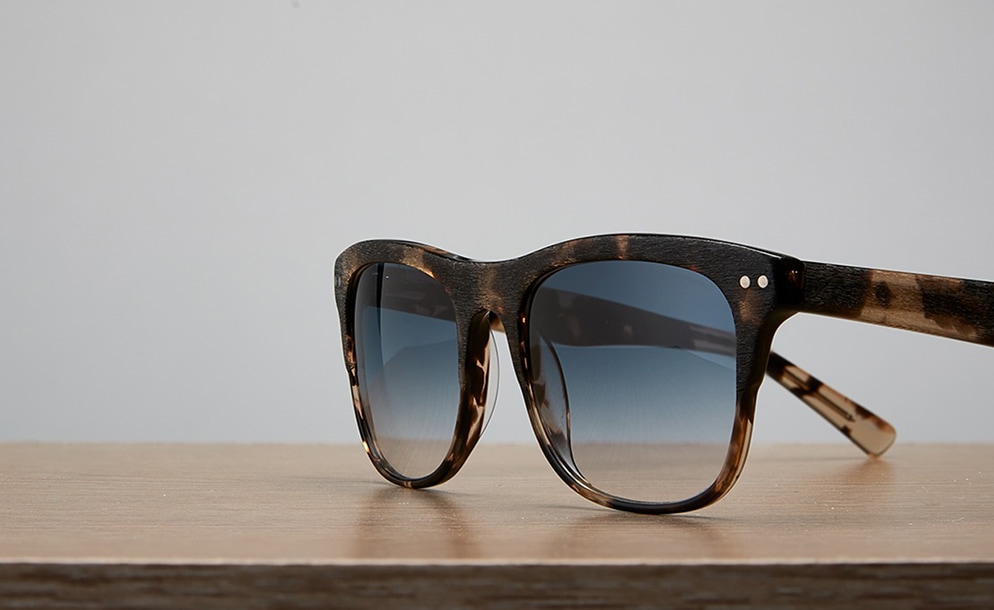 Premium square sunglasses #113435 with light gray tint on a wood table top.
