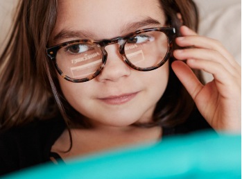 Image of a young kid wearing zenni glasses reading a tablet. 