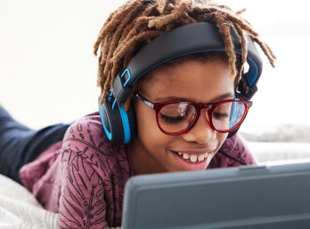 Image of a pre-teen kid wearing zenni glasses and headphones, playing on a tablet.