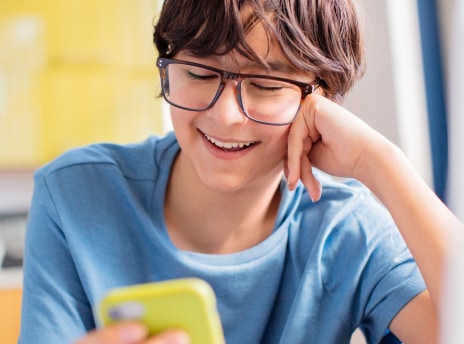Image of a teenage kid wearing zenni glasses and smiling with their phone. 