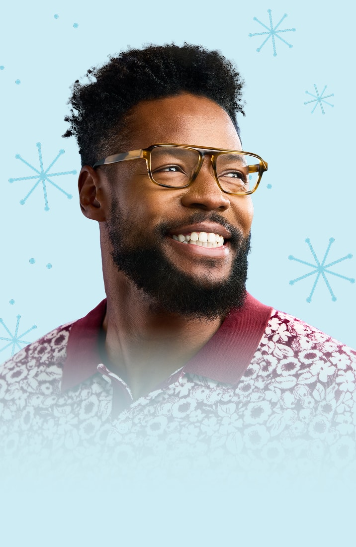 A man with dark brown curly hair and a beard, wearing tortoiseshell aviator glasses, on a light blue background with a star or snowflake motif.