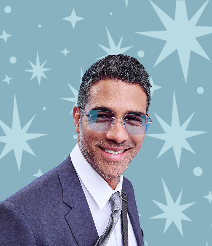 A man with salt and pepper hair wearing rimless square glasses with a blue tint, on a blue background with a starburst motif.