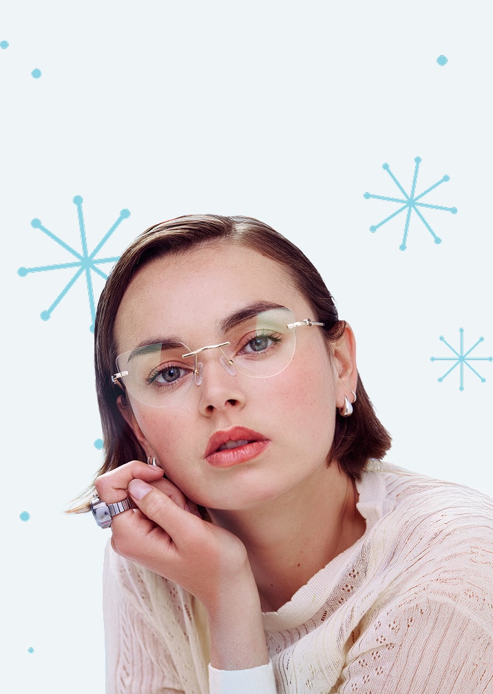 A woman with straight short brown hair wearing cat-eye rimless glasses, on a pale blue background with a star or snowflake motif