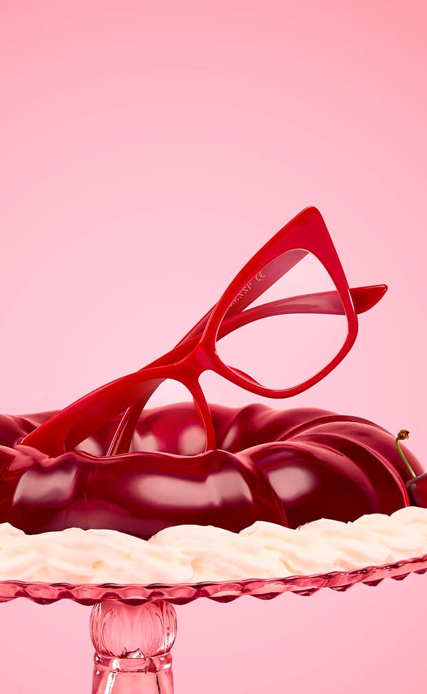 A pair of red eyeglass frames resting on top of a glossy cherry dessert.