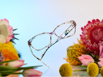 A pair of colorful, translucent floral eyeglasses, floating against a soft pastel blue and pink gradient background, surrounded by vibrant flowers.