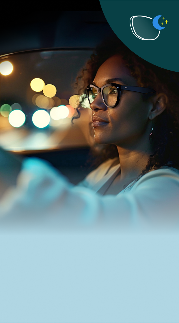A woman wearing glasses drives at night, with soft city lights reflecting in the car window. The photo emphasizes lenses designed to reduce glare and enhance clarity in low-light driving conditions.