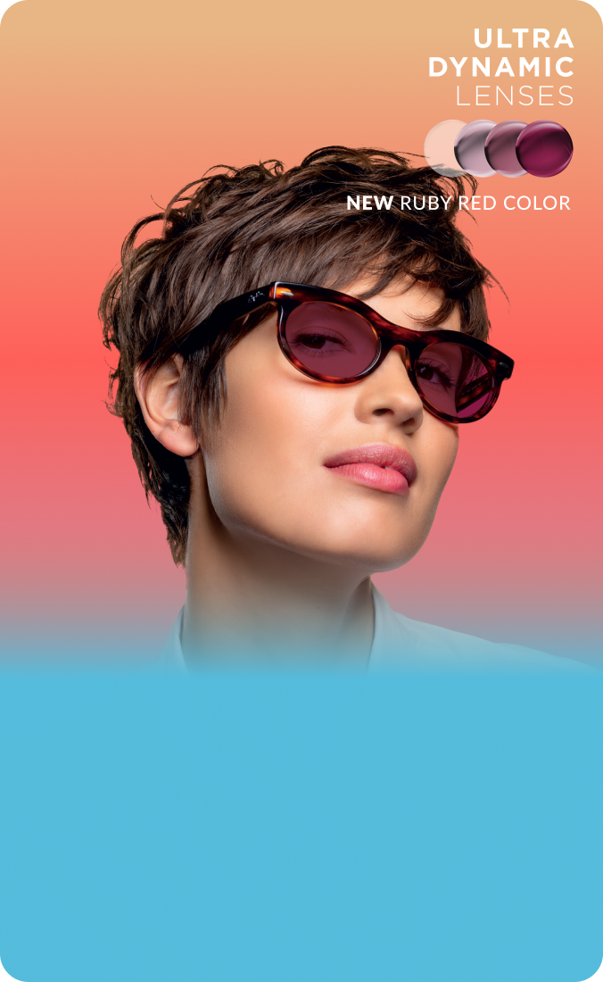 A woman in tortoiseshell glasses with ruby red Transitions Gen S lenses that change from clear to dark.