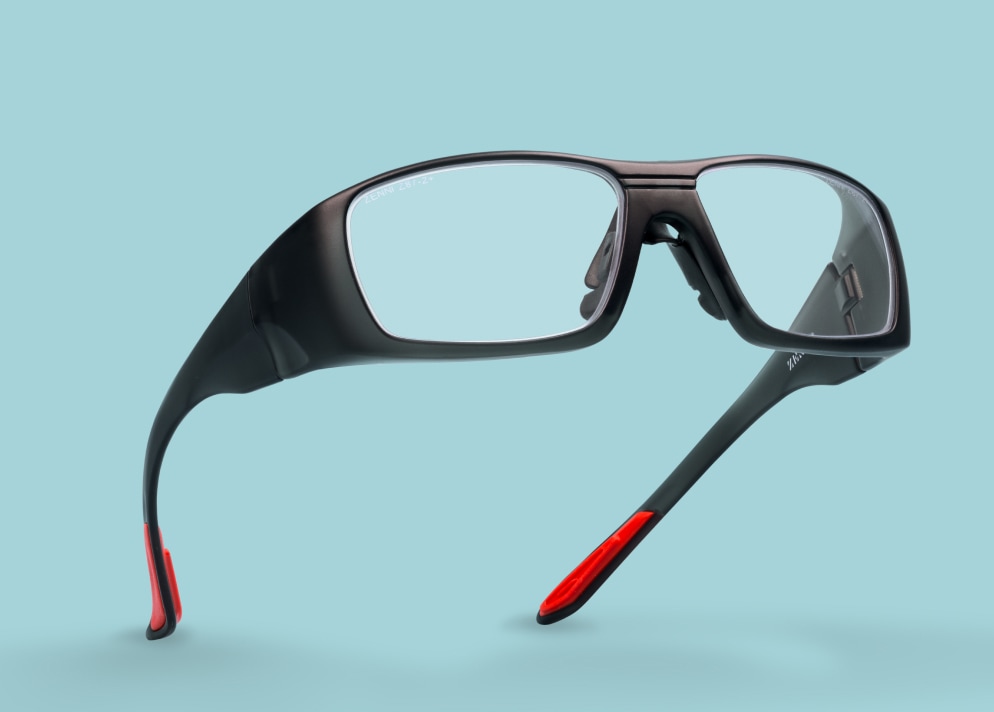 Black Zenni safety glasses with red arm tips on a light blue background.