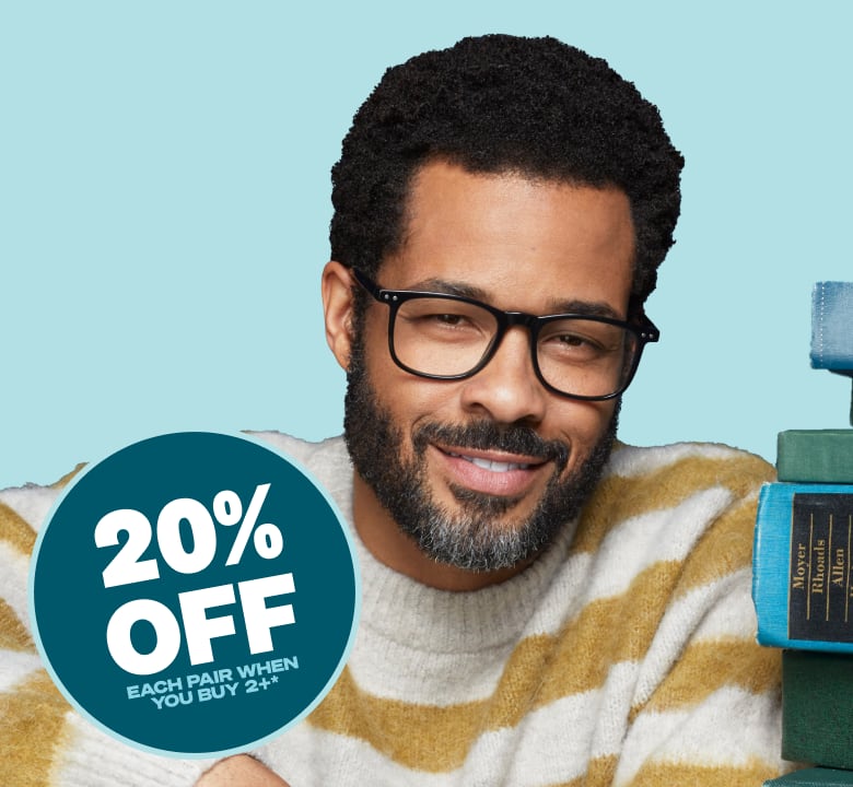 A man with short curly hair and a beard wearing readers glasses smiles at the camera. Next to him, a circular badge contains the text "20% OFF EACH PAIR WHEN YOU BUY 2+" and it is placed against a light blue background. To his right, there is a stack of books in green and blue tones.