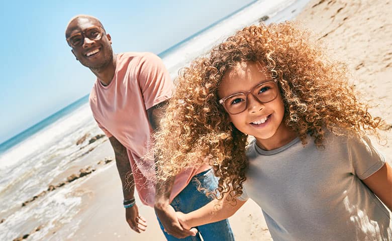 An adult and child wearing Zenni optical frames with Trivex lenses at a beach.