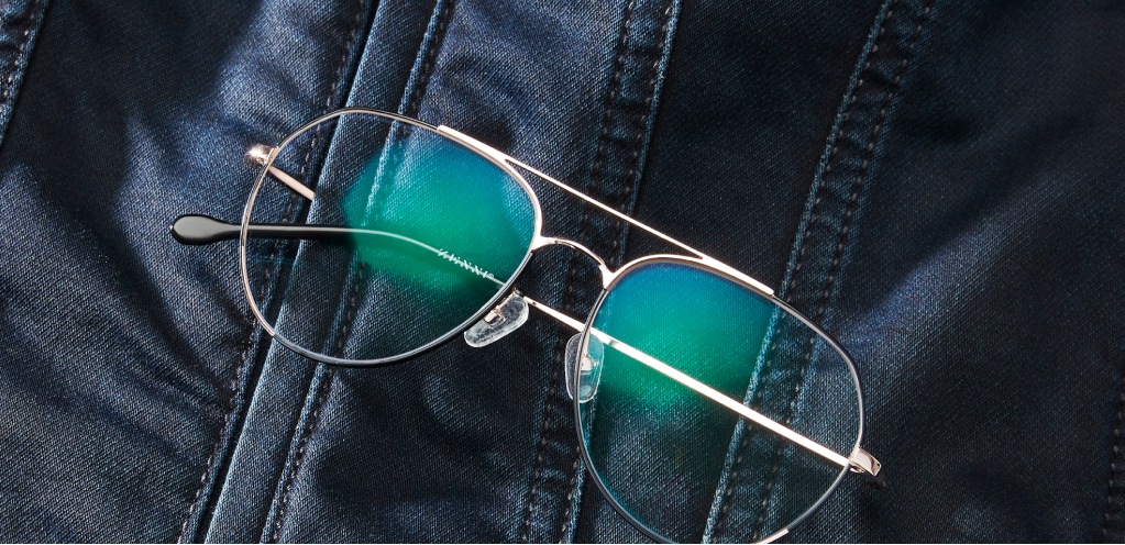 Image of a pair of Zenni aviator glasses with a temple arm tucked into a denim jacket, with a green reflection in the lenses.
